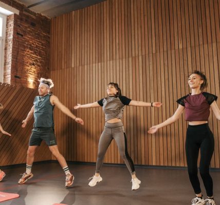 Group of adults doing jumping jacks in modern gym interior.