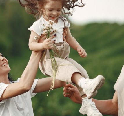 Happy family enjoying playful outdoor moment, lifting child in summer day.